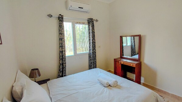 A bedroom with a bed, a bedside table, a mirror, and a window with curtains.