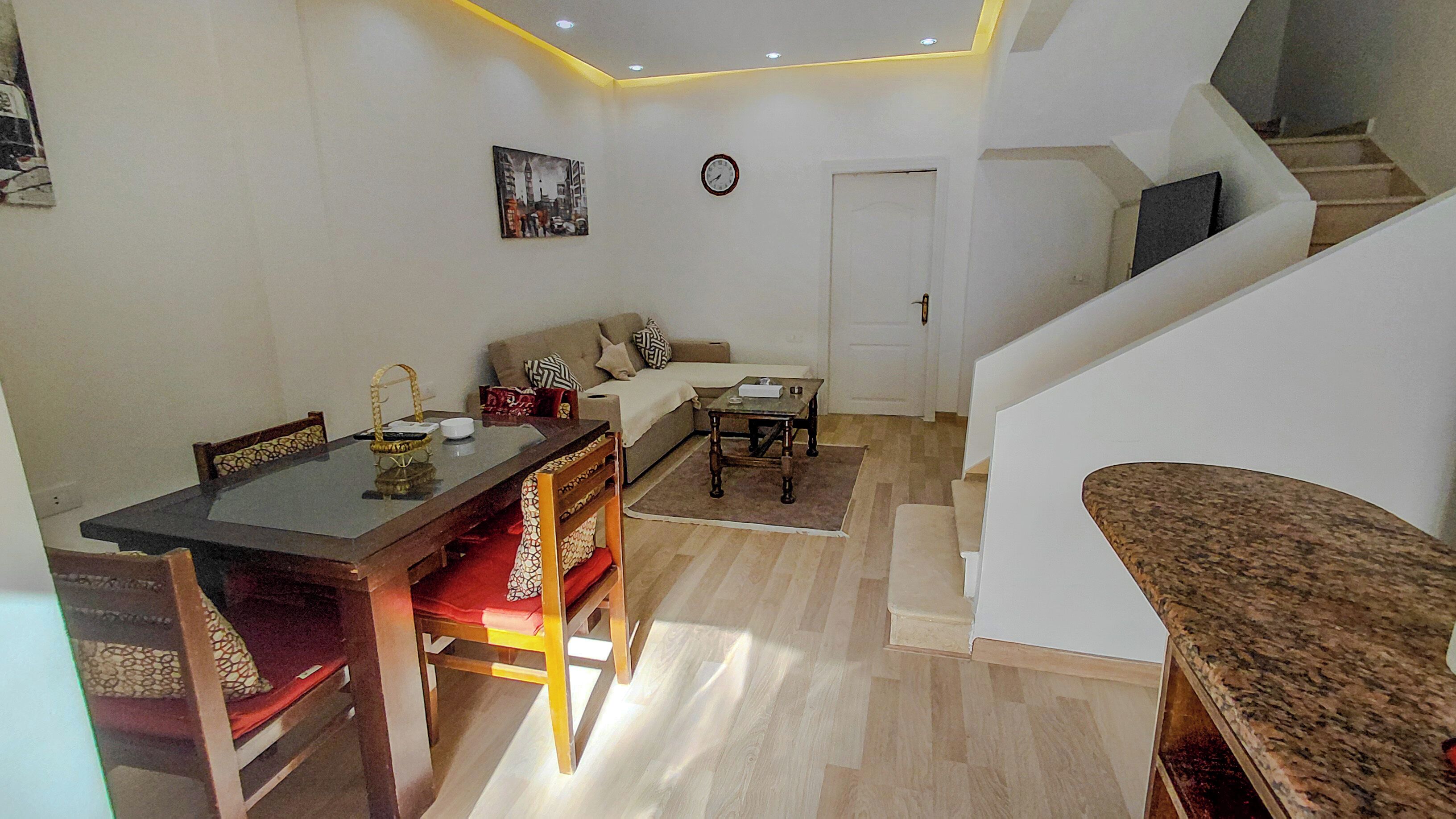 A modern living room with a dining area, a staircase, and a clock on the wall.