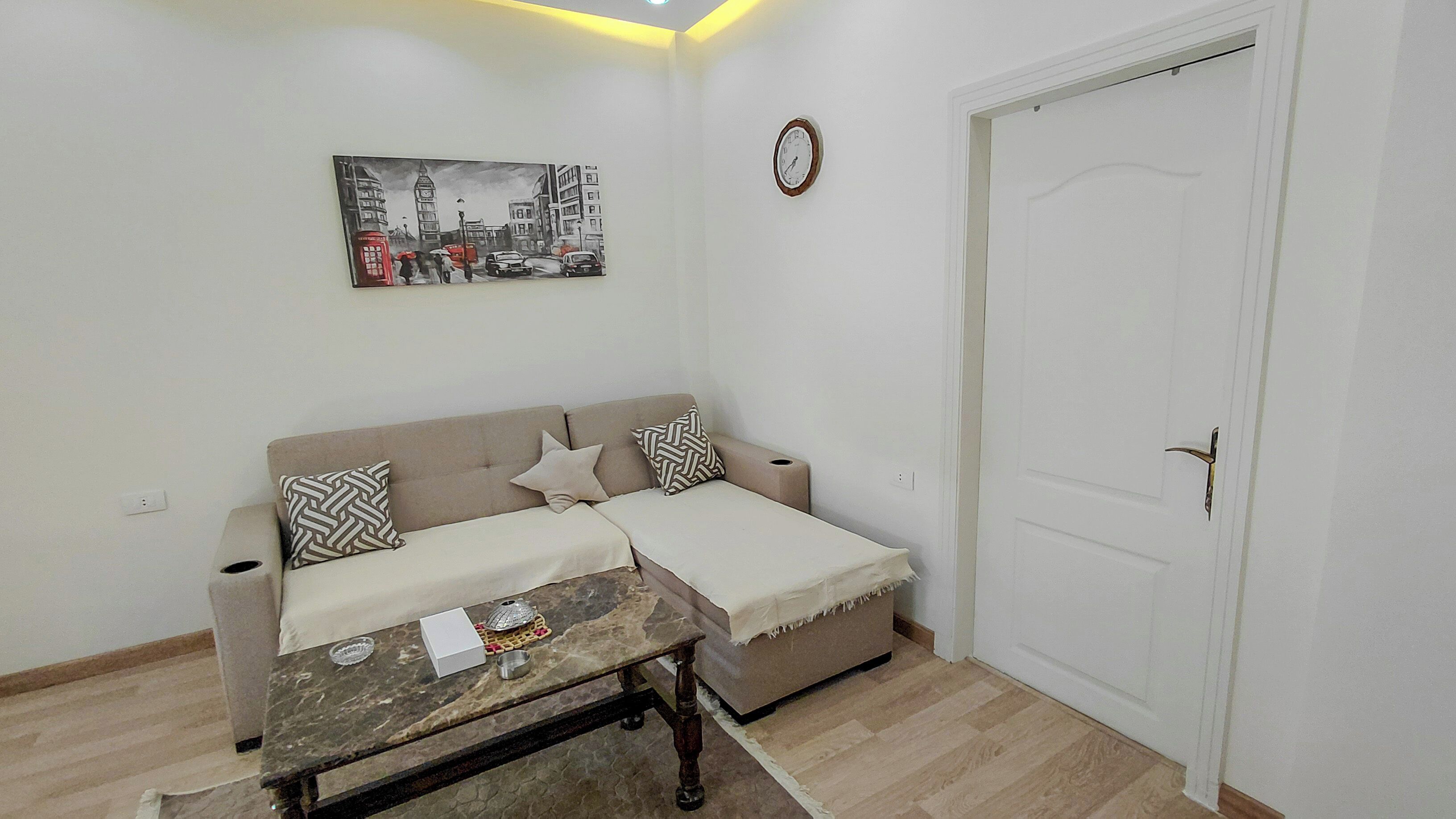 A living room with a sofa, a coffee table, a painting, a clock, and a door.