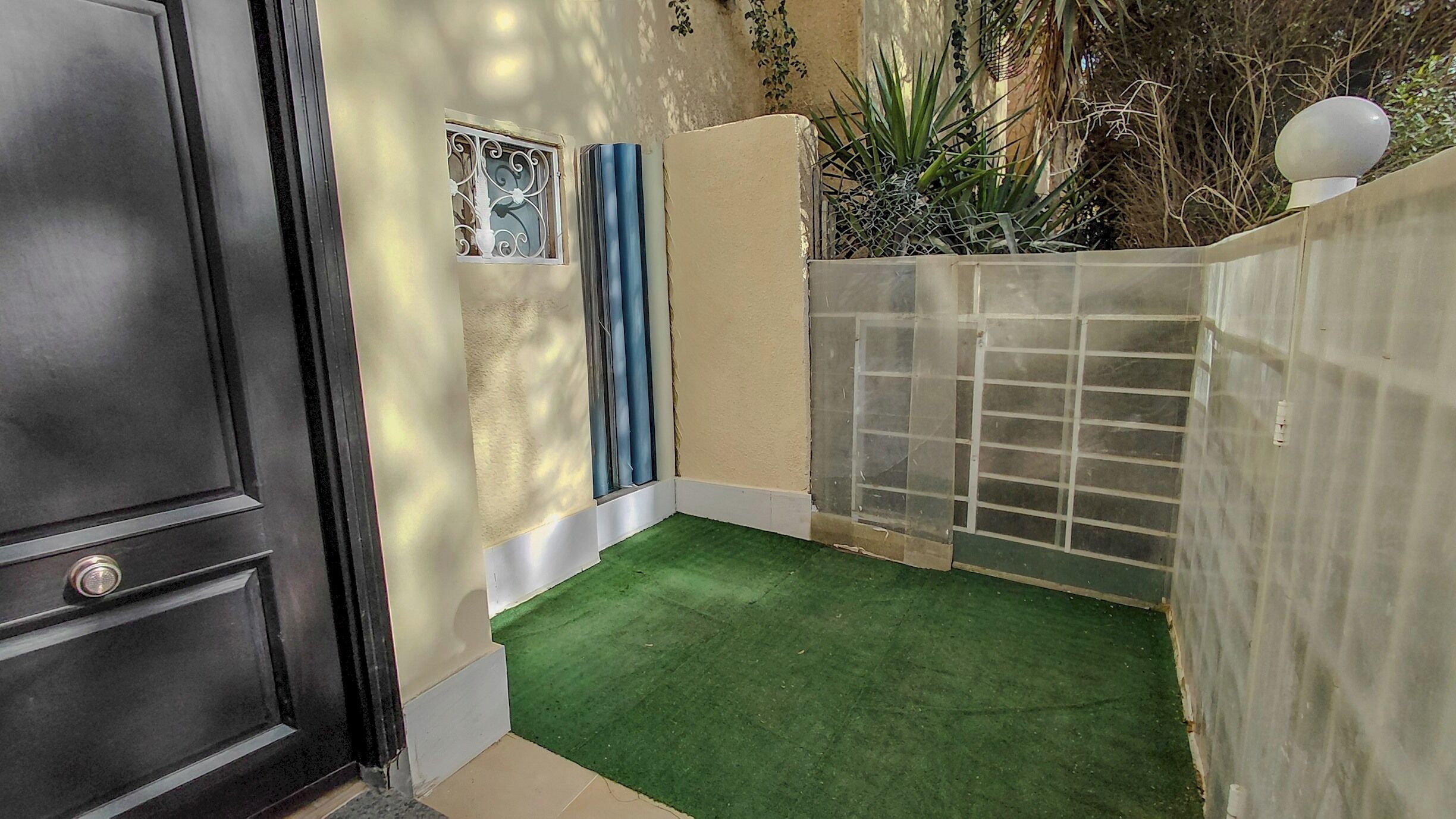 A small enclosed outdoor area with artificial turf, a metal gate, and a potted plant.