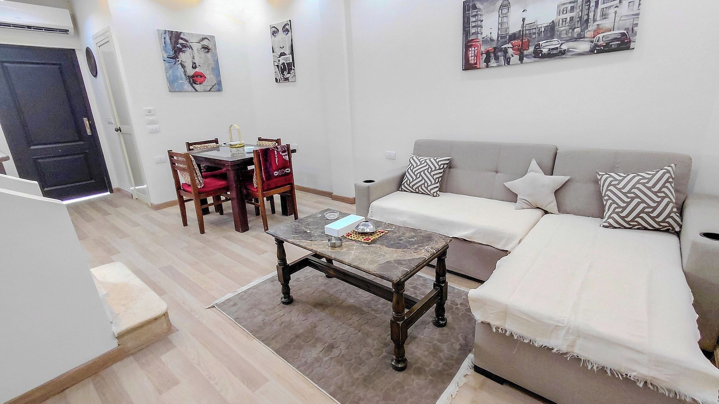 Un salon comprenant un canapé, une table basse, une table à manger avec des chaises et des œuvres d’art accrochées aux murs.