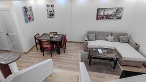 A living room with a dining table, chairs, a sofa, and a coffee table. There are wall art pieces and a door.