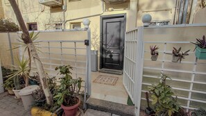 A gated entrance with a door, potted plants, and a small outdoor area with a mat.