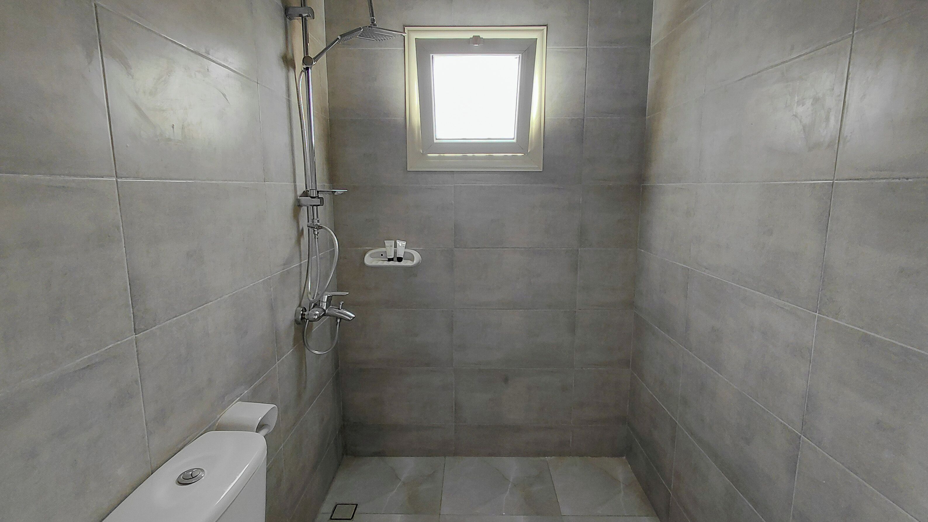 A small, tiled shower room with a window, a toilet, and a showerhead.