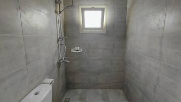 A small, tiled shower room with a window, a toilet, and a showerhead.