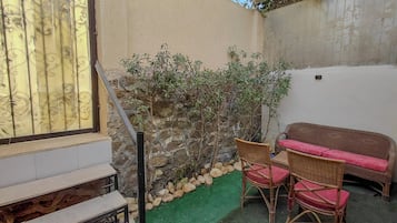 A small outdoor seating area with wicker furniture and a stone wall.