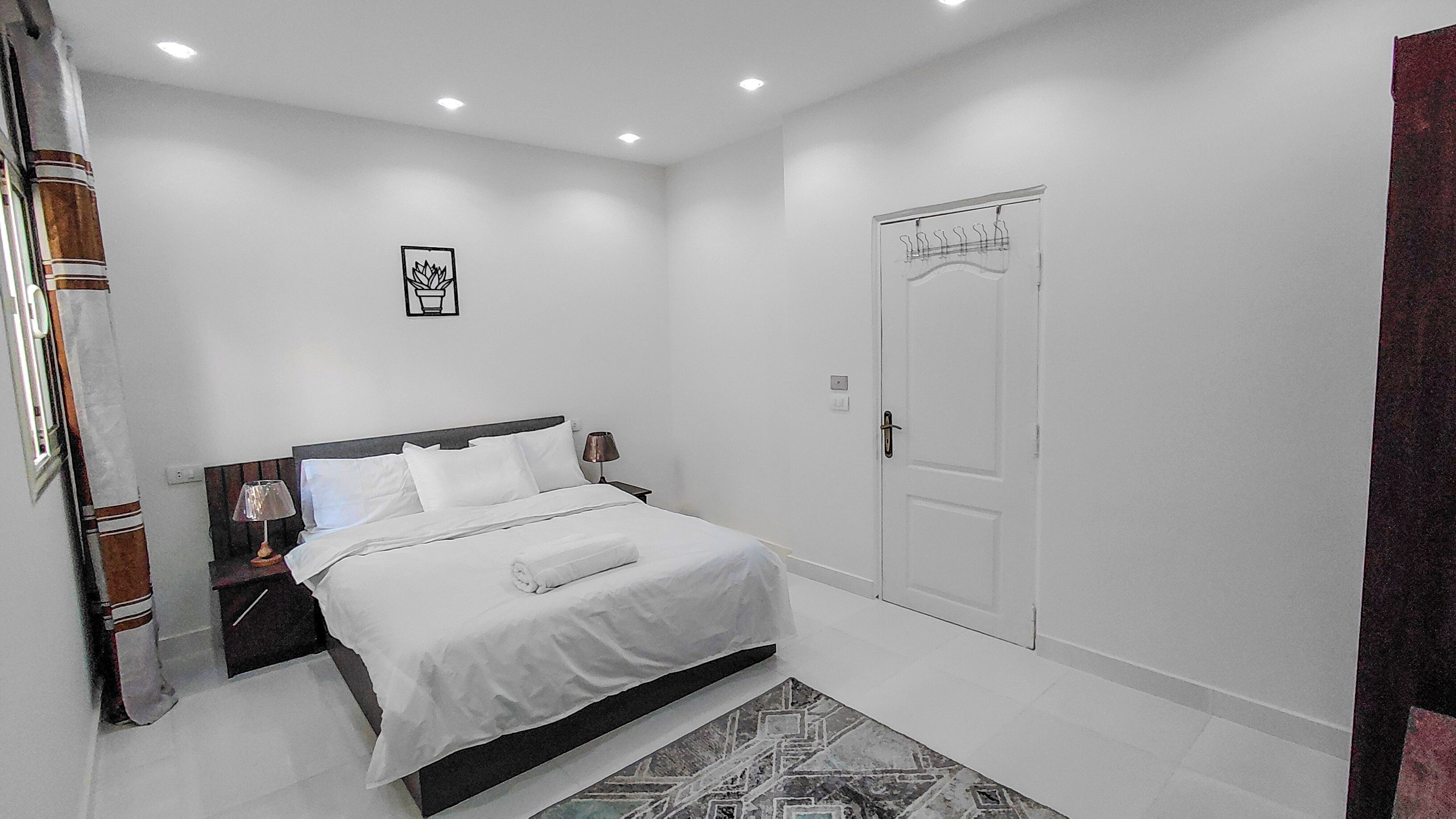 A bedroom with a bed, bedside tables, a door, and a patterned rug.