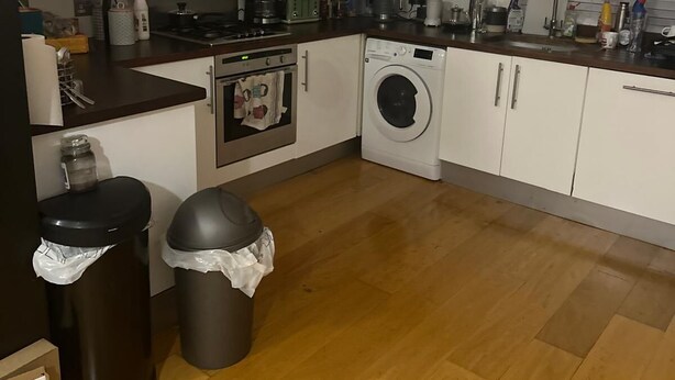 Une cuisine compacte avec des meubles blancs, une hotte en acier inoxydable, un lave-linge et une poubelle.
