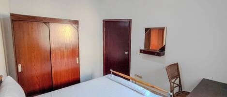 A bedroom with a bed, a wooden wardrobe, a mirror, and a chair.