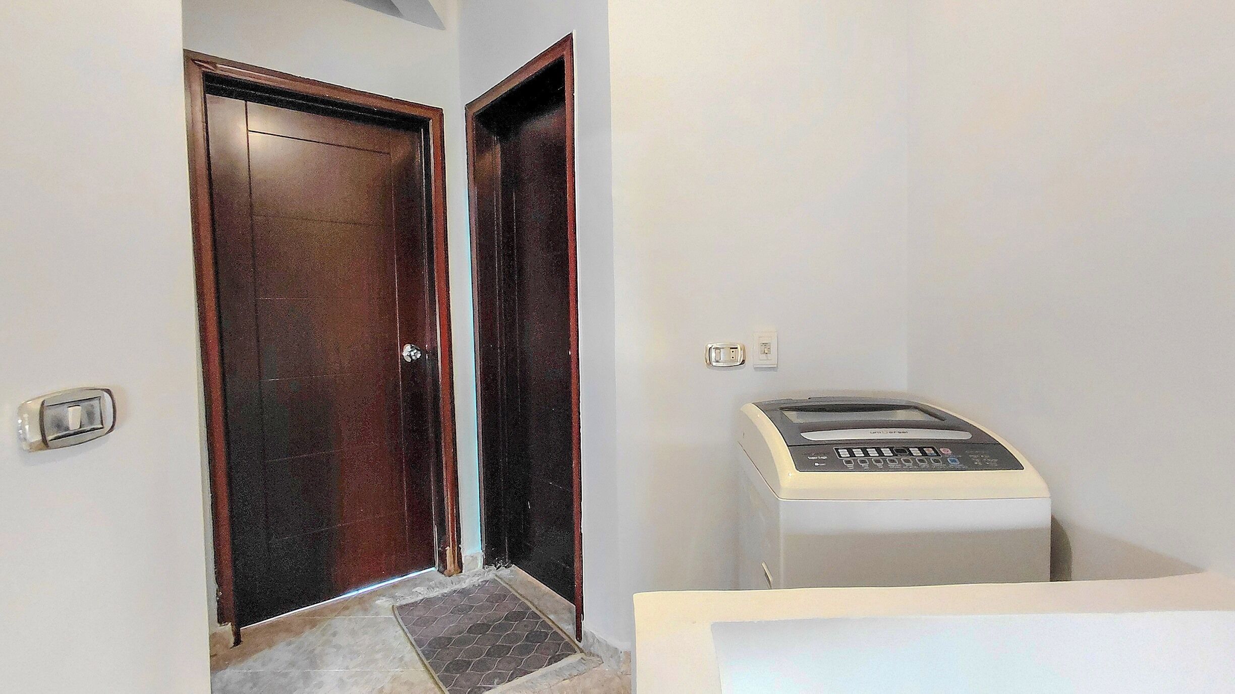 Un couloir étroit avec une porte en bois et un petit objet rectangulaire blanc sur le côté droit.