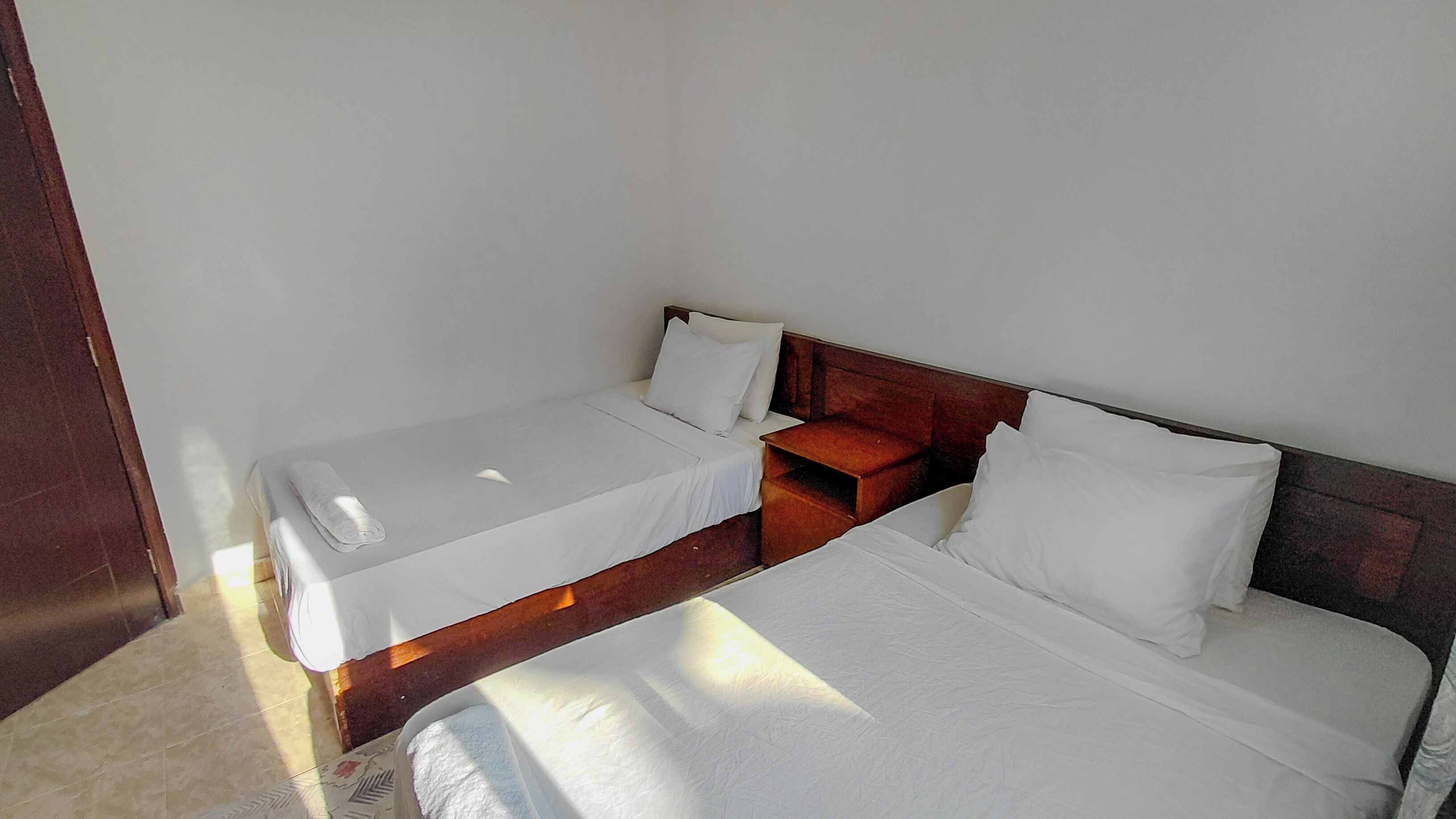 A single-bed room with a wooden headboard, a bedside table, and a window providing natural light.