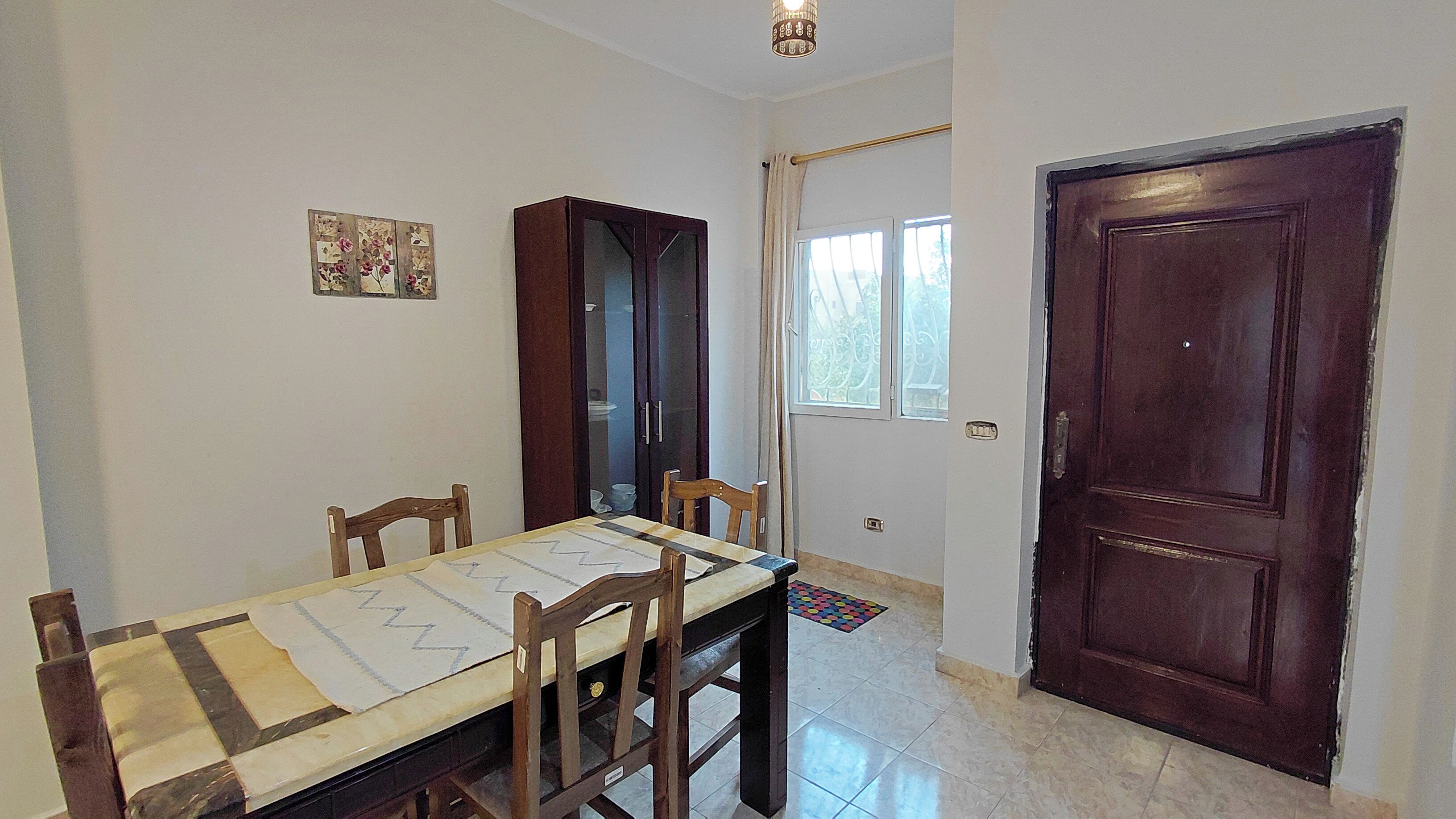 A dining area with a table, chairs, a cabinet, a door, and a window.