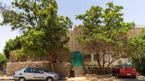 Un edificio con puerta verde, pared de piedra y dos coches aparcados.