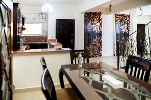 A dining area with a glass-top table, wooden chairs, and a kitchen area with a sink and cabinets. - 575 · 4BR Townhouse, 3 Bath, TV, Backyard (Sheikh Zayed City)