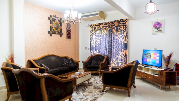 Una sala de estar con sofá, sillones, mesa de centro, televisor y decoración en la pared.