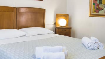A neatly made bed with white linens and towels, a wooden headboard, a bedside table with a lamp, and a painting on the wall.
