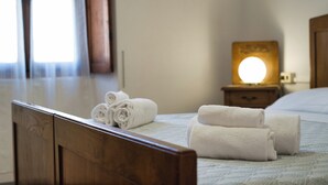 A neatly made bed with rolled white towels, a bedside table with a lamp, and a window with curtains.