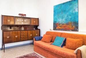 Ein Wohnzimmer mit einem Holzkabinett, einer Couch mit Kissen und einem großen abstrakten Gemälde an der Wand.