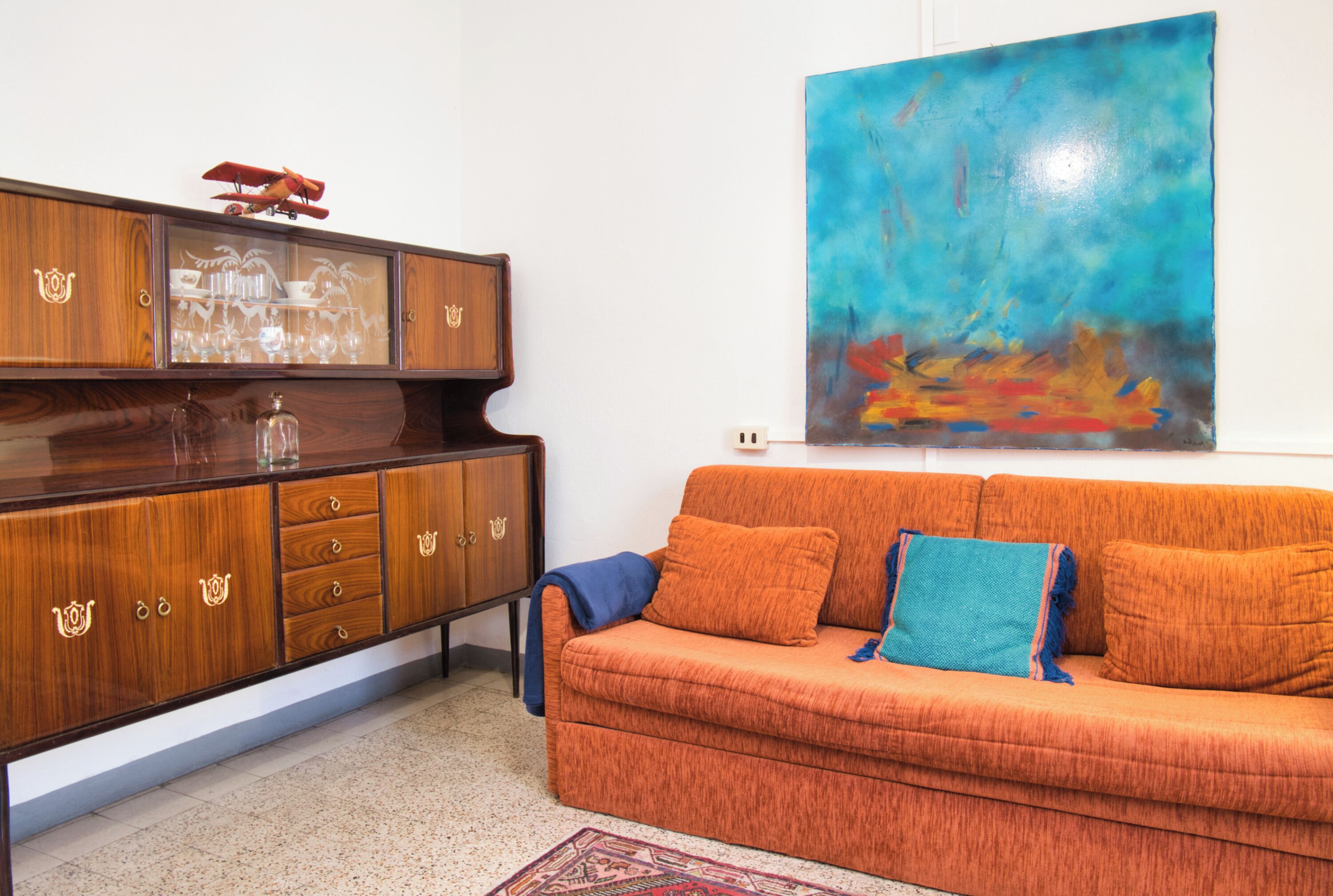 A room with a wooden cabinet, a sofa, and a large abstract painting.