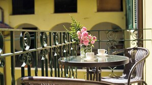 A balcony with a table, chairs, a vase with flowers, and a cup.
