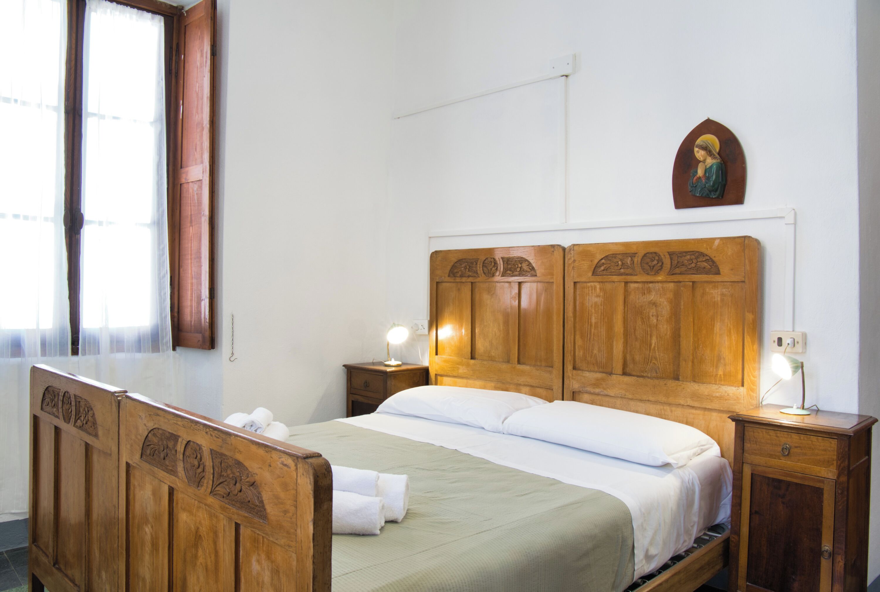 Un lit en bois avec une tête de lit, deux tables de chevet, une lampe fixée au mur et une fenêtre avec des rideaux.