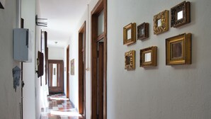 A hallway with a checkered floor, wooden doors, and a series of framed pictures on the wall.