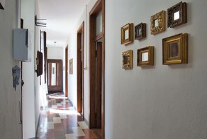 A hallway with a checkered floor, wooden doors, and a series of framed pictures on the wall.