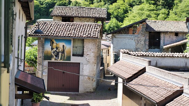 A courtyard with traditional buildings, a mural, and a potted plant.
