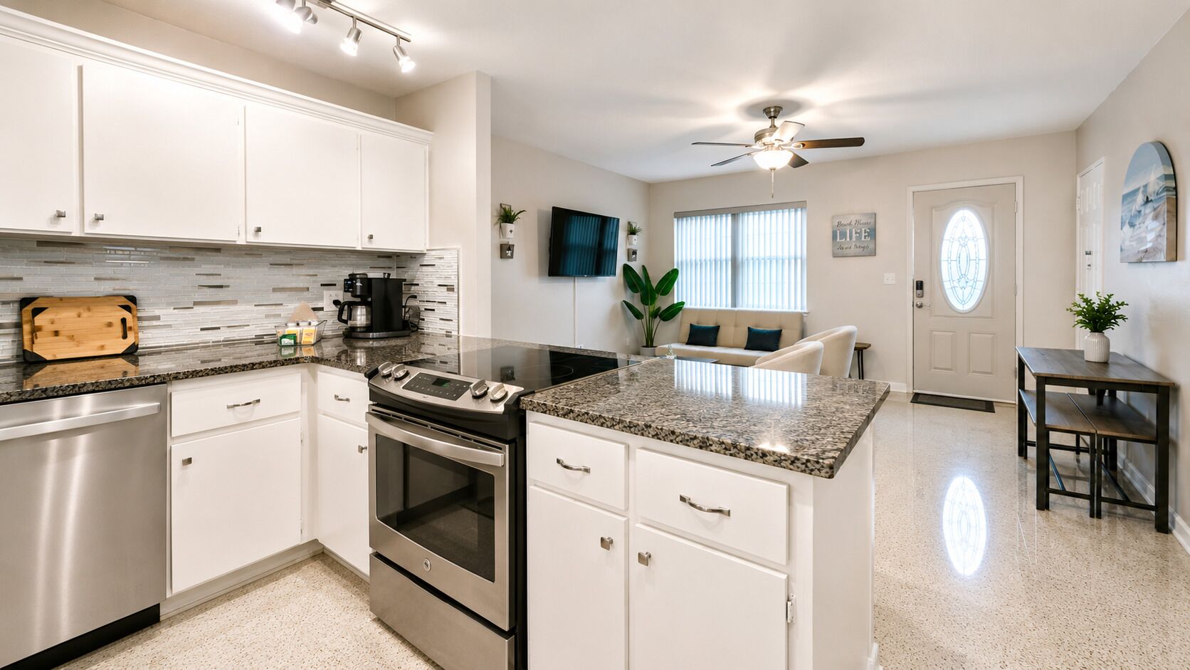 A modern kitchen with stainless steel appliances, white cabinetry, and a granite countertop.