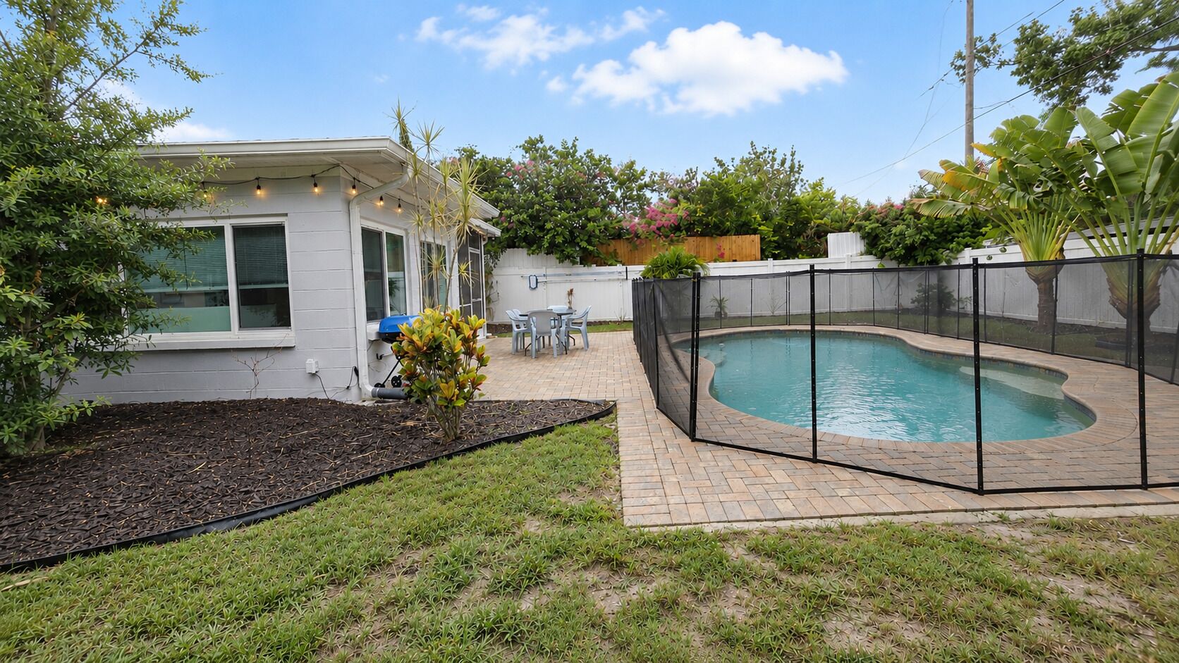 A backyard with a swimming pool, a patio with chairs, and a small garden area.