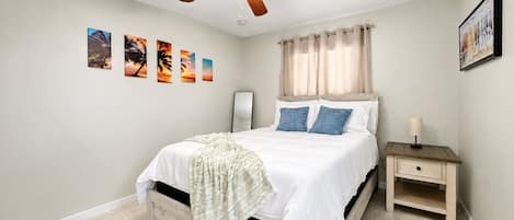 A bedroom with a bed, a nightstand, a ceiling fan, and wall art.