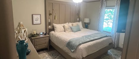 A bedroom with a bed, bedside tables, a nightstand, a ceiling fan, and a window with curtains.
