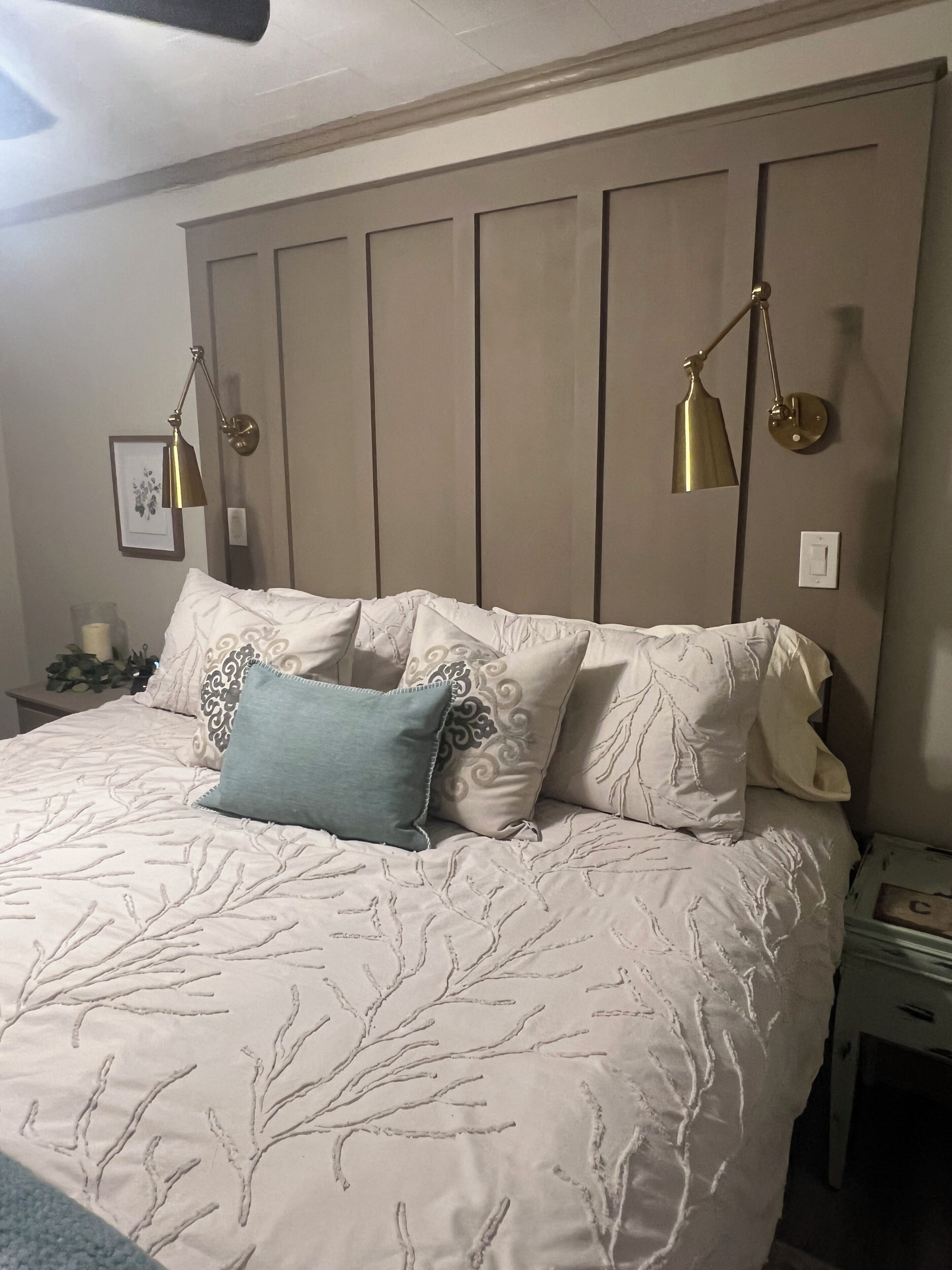 A bedroom with a large bed, two wall-mounted lamps, and a framed picture on the wall.