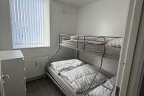 Quarto com beliche, radiador, janela com persianas e porta.
