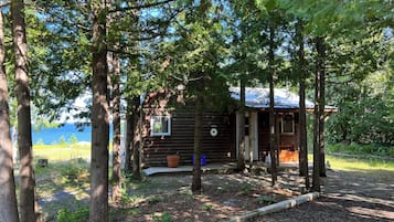 Une cabane dotée d’un petit porche, entourée d’arbres et offrant une vue sur une étendue d’eau.