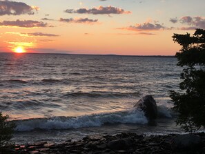Un coucher de soleil sur une étendue d’eau, avec des vagues qui se brisent sur une côte rocheuse.