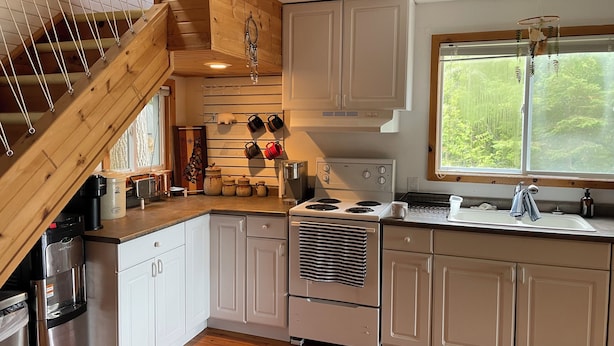 A kitchen with white cabinets, a stainless steel refrigerator, a stove, and a window with a view of greenery. - Welcome to The Cedars.
Beautifully maintained waterfront quaint log cabin (Northeastern Manitoulin and the Islands)