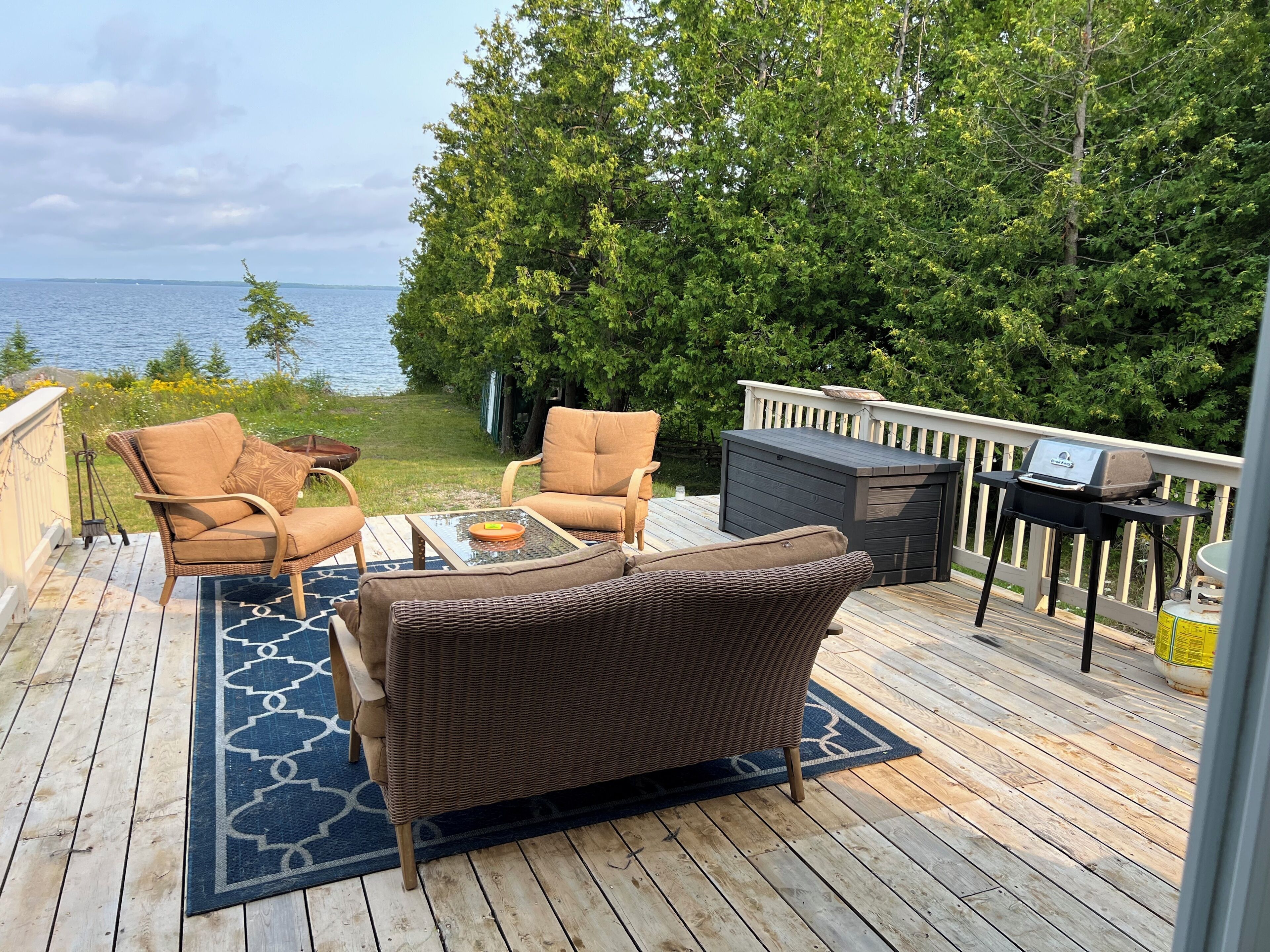 A deck with wicker furniture, a grill, and a view of the water.
