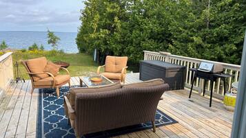 A deck with wicker furniture, a grill, and a view of the water.