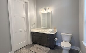 Ein Badezimmer mit weißer Tür, dunklen Schränken, einer weißen Toilette und einem Spiegel mit Beleuchtung.