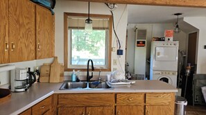 A kitchen with wooden cabinets, a sink, a window with blinds, a washing machine, and a 'NO SMOKING' sign.