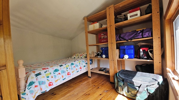 Una habitación pequeña con una cama individual, estantes de madera y una ventana.