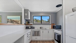 Une cuisine moderne avec des meubles blancs, un lave-vaisselle en acier inoxydable, un four encastré et une fenêtre donnant sur des maisons.