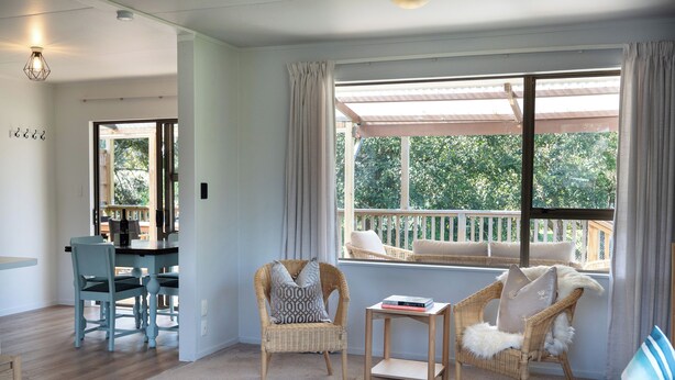 Un salon chaleureux avec un coin repas, de grandes fenêtres avec des rideaux et une vue sur la verdure environnante.