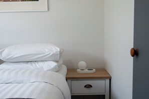 A neatly made bed with white bedding, a bedside table with a lamp, and a drawer. - Calden Cottage - Ngunguru Holiday Home (Whangarei)