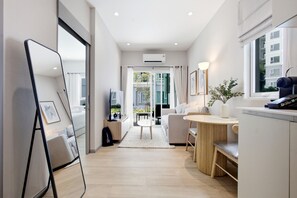 A modern hotel room with a kitchen area, a dining table, and a large window providing a view of the outdoors. - Title Serenity Naiyang: pool access (Thalang District)