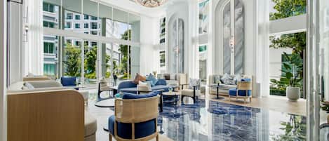 A spacious hotel lobby with a high ceiling, large windows, and a reflective marble floor.