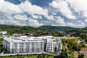 A multi-story hotel with a modern architectural design, surrounded by lush greenery and a mountainous backdrop. - Title Serenity Naiyang: pool access (Thalang District)