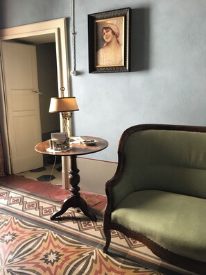 A room with a green upholstered chair, a round table with a lamp, and a framed picture on the wall. - Casa Briga: A historic 19th-century noble residence. (Montesilvano Colle)