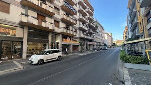 Ein mehrstöckiges Gebäude mit Balkonen, ein weißes Auto auf der Straße geparkt und Geschäfte mit Beschilderung.